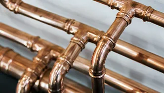 Close-up view of several copper pipes with joints and elbows, arranged parallel against a light background.